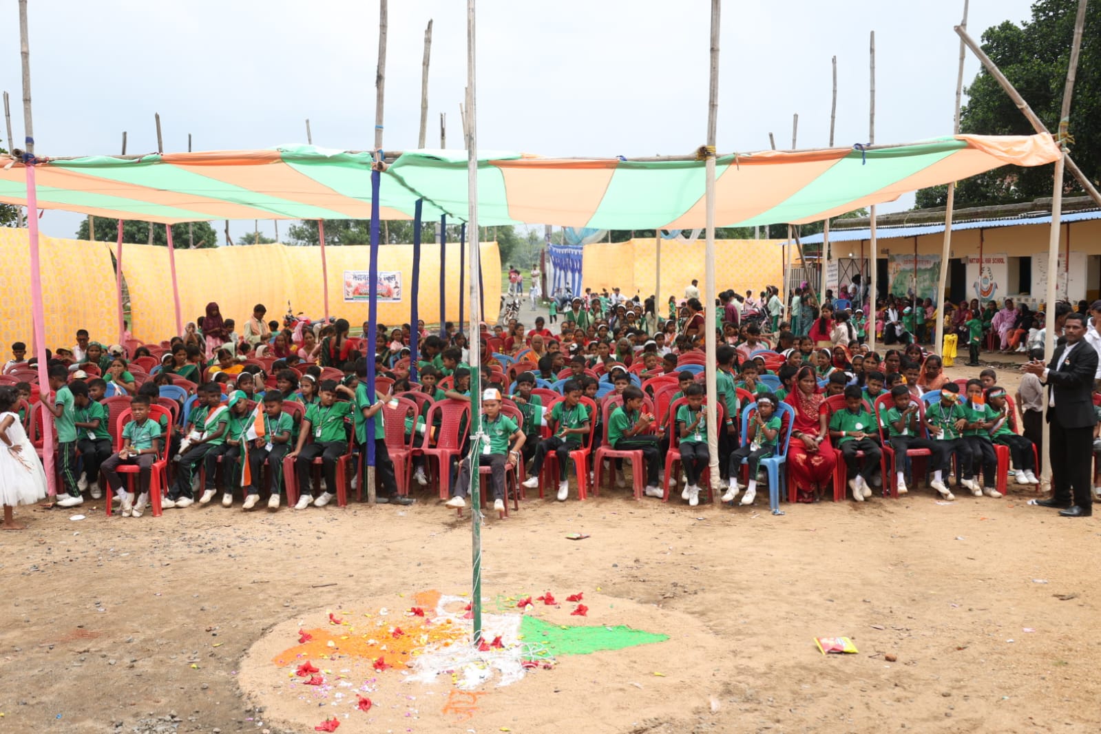 Wide photograph of the Independence Day rally at N.H.S. Bagodar — students carrying the school banner and Indian flags.